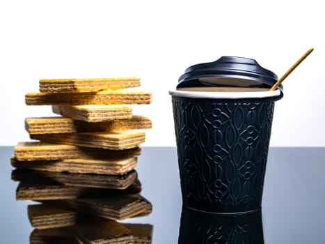 Black paper disposable cup for coffee drinks and waffle cookies on the table. Coffee drink Waffle dessert. Street Cafe. Paper cup. Disposable tableware. Dishes for hot drinks. Tea. Table.