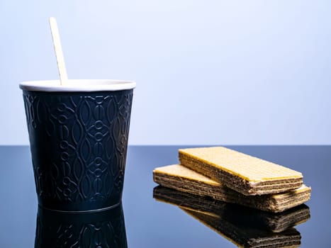 Black paper disposable cup for coffee drinks and waffle cookies on the table. Coffee drink Waffle dessert. Street Cafe. Paper cup. Disposable tableware. Dishes for hot drinks. Tea. Table.