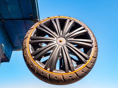 A car wheel attached to the roof of a building against the blue sky. Tire service. Car tire. Vehicle spare part. Customer Service. Repair and service. Metal detail. Mechanic repairman. Master.
