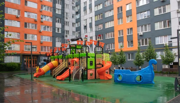 A courtyard of high-rise buildings with a new modern colorful and large playground on a rainy summer day without people. Empty outdoor playground. A place for children's games and sports