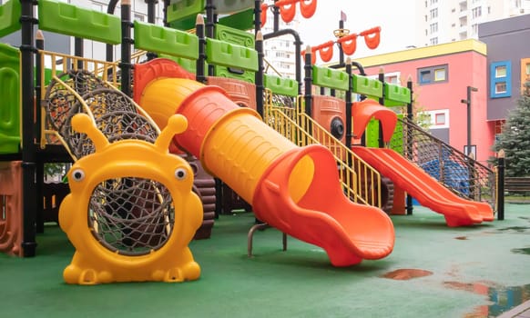 A courtyard of high-rise buildings with a new modern colorful and large playground on a rainy summer day without people. Empty outdoor playground. A place for children's games and sports