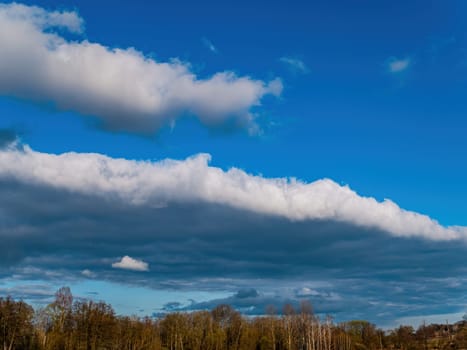 Forest horizon against a blue sky with white clouds. Cloudy horizon. Blue sky. Forests and meadows. Natural season. Spring season. Rain clouds. Background image.