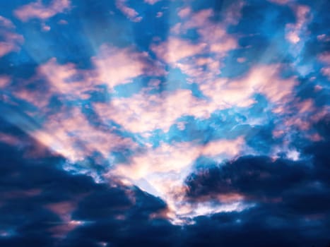 Sunbeams of pink evening sunset on cloudy sky. Sun rays. Pink evening sunset. Blue skies. Cloudy sky. Natural landscape. Natural background. Atmospheric phenomenon. Beauty.