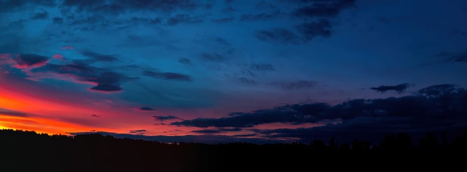 Red sunny sunset with thunderclouds on the horizon. Sky with clouds. Sunny sunset. Cloudy horizon. Forest in the dark. Evening twilight. Night time. Weather. Natural landscape. Panoramic photo.