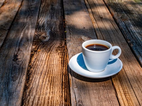 White cup with coffee on a wooden table. Coffee drink. Ceramic tableware. Wooden table. Hot drink. Mug for drinks. Street Cafe. Morning breakfast. Caffeine. Leisure activities.