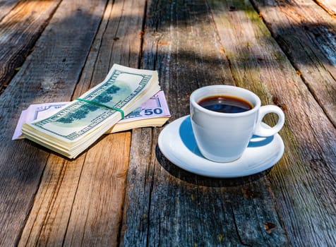A cup of coffee and a bundle of money on a wooden table. Coffee drink. Catering business. American dollars. Banking and finance. Commercial activity. Financial transaction. Business.