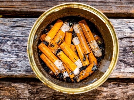 Ashtray from a tin can with cigarette butts on a wooden table. Tin can. Ashtray for cigarette butts. Smoking area. Smoker. Drug addiction. Not a healthy lifestyle. Nicotine and tobacco.