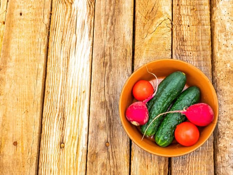 Vegetables cucumbers with tomatoes and radishes in a plate. Green cucumber. Red tomato. Red radish. Vegetable salad. Ceramic tableware. Wooden table. Vegetarian food. Healthy eating.