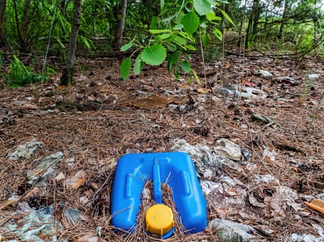 The blue plastic canister is buried in the ground. Container for chemicals. Yellow cover. Automotive chemicals. Environmental pollution. Plastic trash. Ecology. Industrial waste.