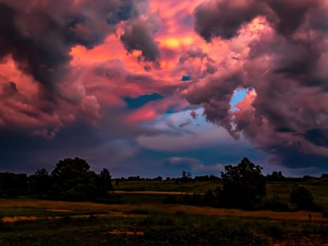 Thunderclouds in the pink rays of the sunset. Cloudy horizon. Fields and meadows. Natural landscape. Climatic conditions. Weather forecast. Storm and hurricane. Green trees. Rain clouds.