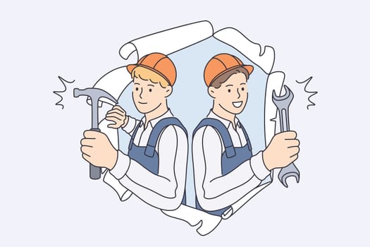 Repairmen during construction work concept. Young smiling men workers in helmets and working uniform standing looking from damaged old wallpapers holding hammers in hands