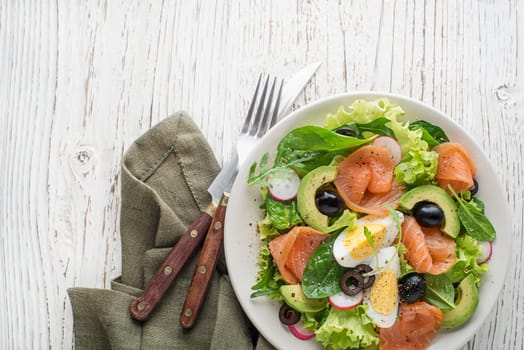 Fresh green lettuce salad with smoked salmon and avocado on wooden background