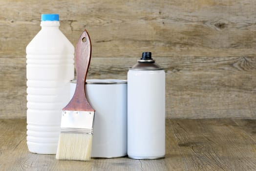 bottle, aerosol, paint pot and brush on wooden table