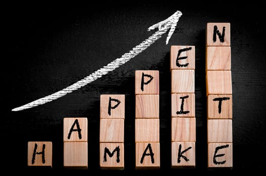 Message MAKE IT HAPPEN  on ascending arrow above bar graph of Wooden small cubes isolated on black background. Chalk drawing on blackboard. Business Concept image.