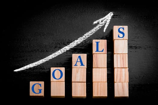 Ascending arrow above bar graph of Wooden small cubes isolated on black background. Chalk drawing on blackboard. Business Concept image.