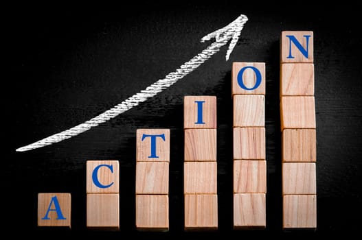Word ACTION on ascending arrow above bar graph of Wooden small cubes isolated on black background. Chalk drawing on blackboard. Business Concept image.