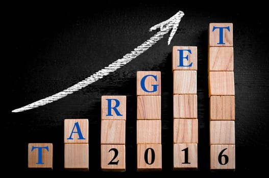 Message TARGET 2016 on ascending arrow above bar graph of Wooden small cubes isolated on black background. Chalk drawing on blackboard. Business Concept image.