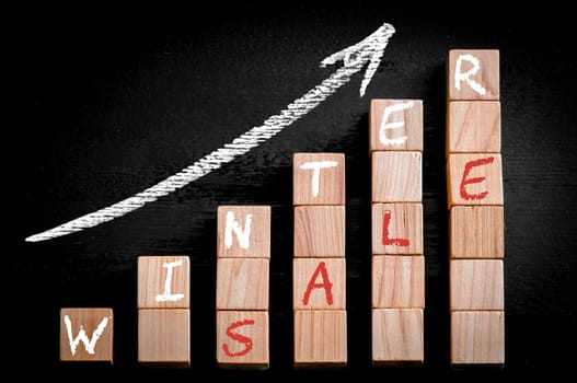 Message WINTER SALE on ascending arrow above bar graph of Wooden small cubes isolated on black background. Chalk drawing on blackboard. Business Concept image.
