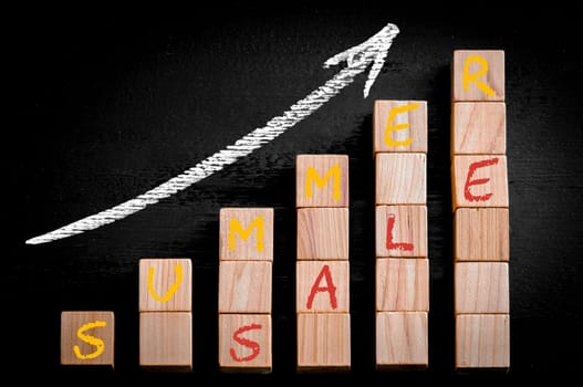 Message SUMMER SALE on ascending arrow above bar graph of Wooden small cubes isolated on black background. Chalk drawing on blackboard. Business Concept image.