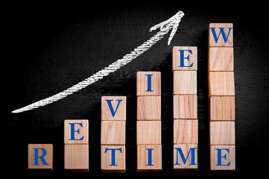 Message REVIEW TIME on ascending arrow above bar graph of Wooden small cubes isolated on black background. Chalk drawing on blackboard. Business Concept image.