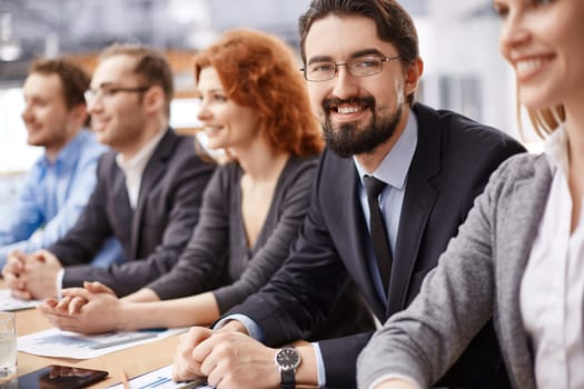 Young businessman sitting among co-workers and looking at camera at conference