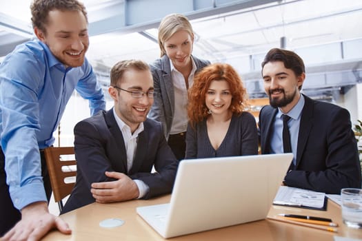 Happy business partners looking at laptop display at meeting