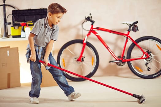 Adolescent boy with mop cleaning floor in garage