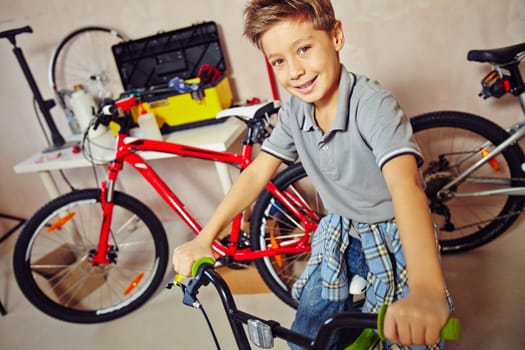 Cute boy sitting on bicycle in garage