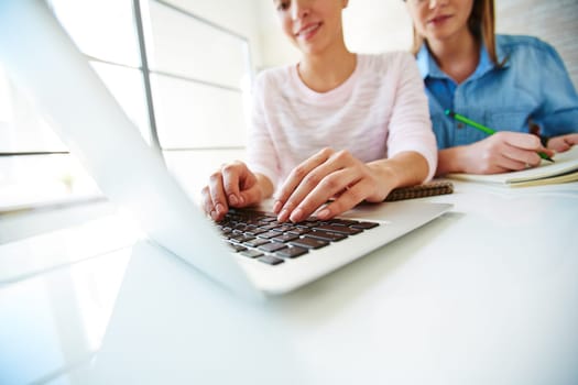 Young female typing on laptop by desk