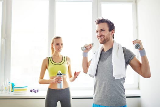 Happy guy exercising with dumbbells with his girlfriend on background