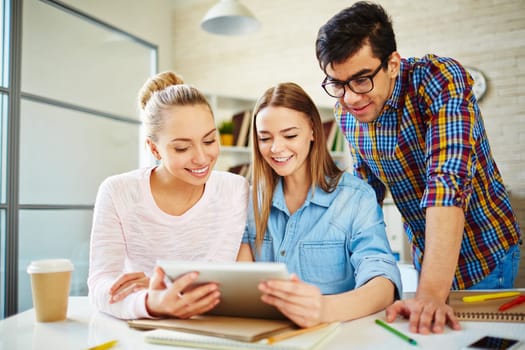 Three happy teenagers looking through data in touchpad