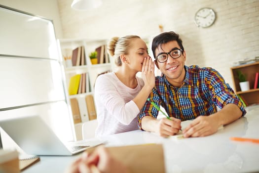Teenage girl whispering fun to attractive groupmate