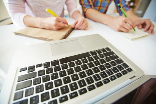 Laptop keypad at workplace on background of two girls making notes
