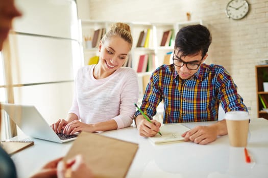 Teenage guy drawing in library while happy girl looking at his picture