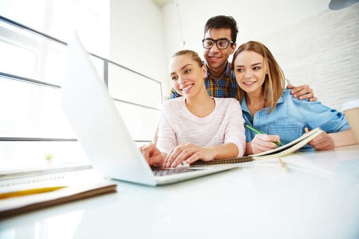 Group of three teenagers looking through data in laptop