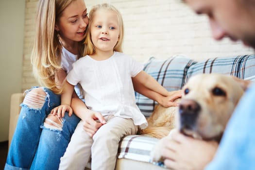 Cute little girl looking at dog with her mother near by