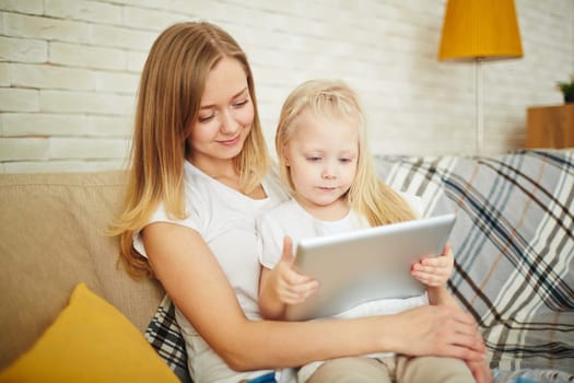 Curious girl with touchpad sitting on the knees of her mother