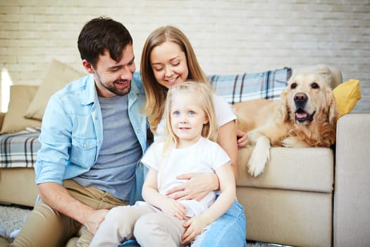 Happy couple and their daughter enjoying home rest with pet on background