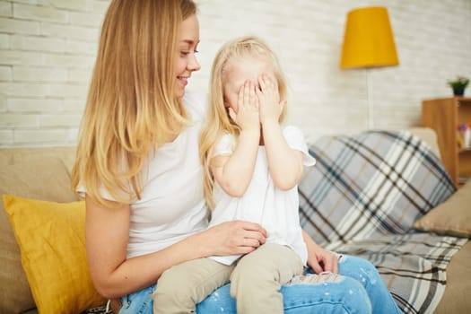 Little girl on her mother’s knees closing her eyes by palms