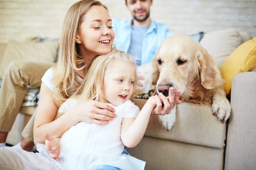 Happy female and her daughter looking at dog with young man on background