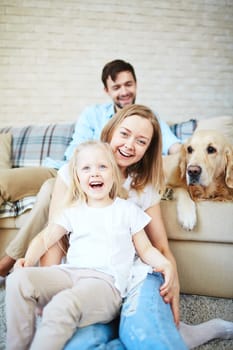 Happy female and little girl laughing with dog and young man on background