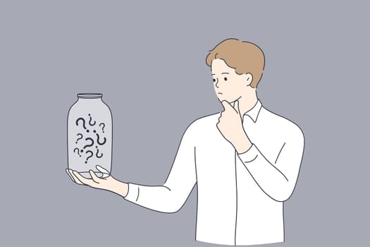 Saving money, crisis, bankrupt concept. Frustrated businessman holding empty glass jar with question marks inside feeling stressed and unhappy with finger on chin isolated over grey background