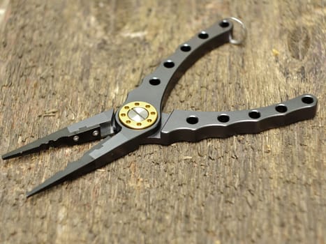 modern fishing pliers on wooden background close-up