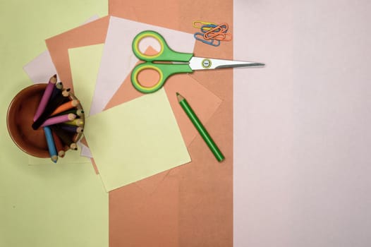 Colour paper, scissors, school stationery supplies, pencils, paint, and ruler lying on table. Origami DIY tutorial for kids background. Back to school concept. Directly above. Flat lay.