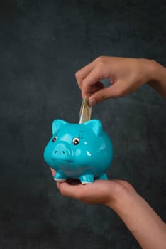 Putting money into a blue piggy bank, empty copy space for text