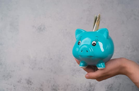 Putting money into a blue piggy bank, empty copy space for text