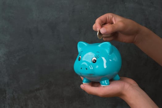 Putting money into a blue piggy bank, empty copy space for text