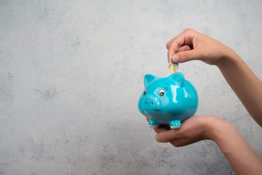 Putting money into a blue piggy bank, empty copy space for text