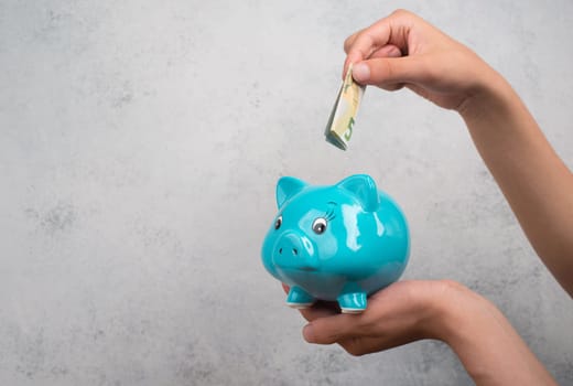 Putting money into a blue piggy bank, empty copy space for text