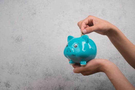 Putting money into a blue piggy bank, empty copy space for text